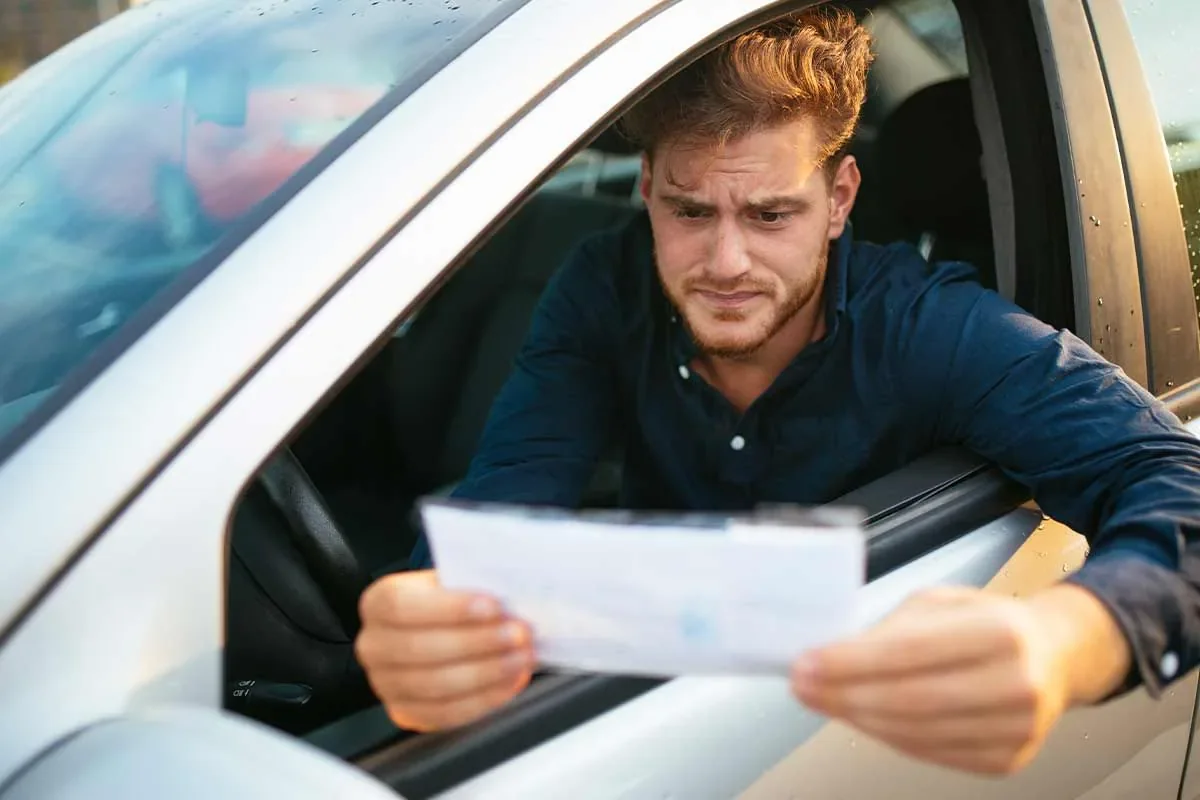 Motorista olhando preocupado para uma notificação de multa